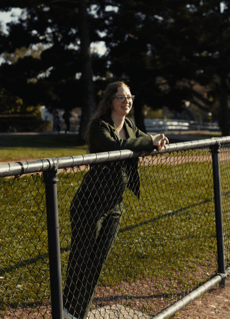 Steph Murphy, dietitian at All Bodies Services, smiling and leaning against a park fence