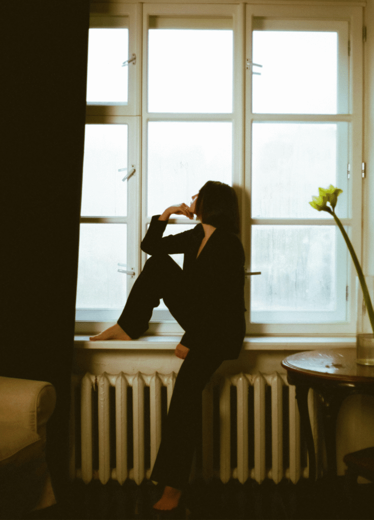 Woman sitting on a windowsill, resting her chin on her hand, looking out the window